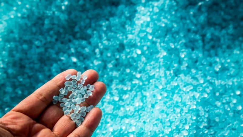Una mano tiene delle palline trasparenti sopra una superficie ricoperta da palline di plastica blu simili.