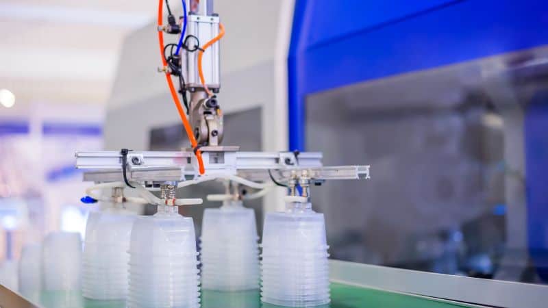 Un braccio robotico impila contenitori di plastica trasparente in un ambiente di produzione automatizzato.