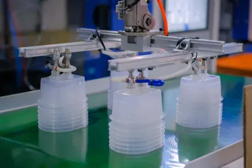 Robot gripper handling stacks of clear polypropylene food containers on a conveyor