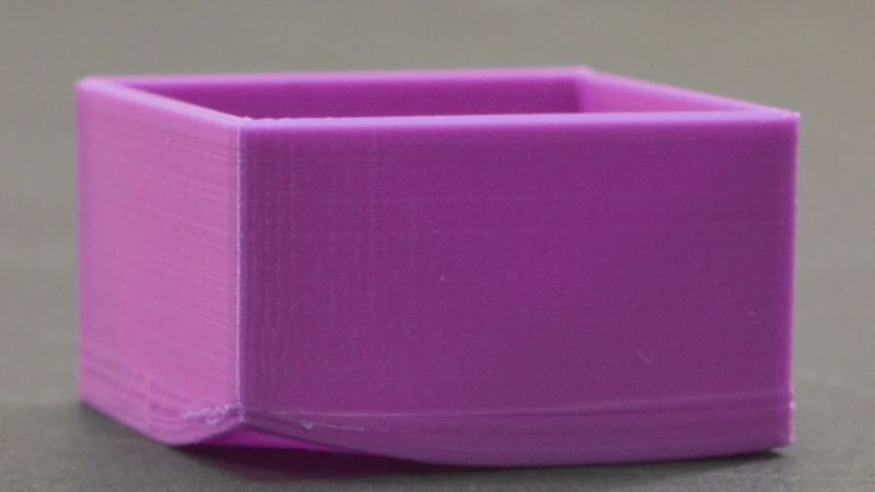 Un mic dreptunghi violet imprimat 3D cu linii de straturi și o bază neuniformă.