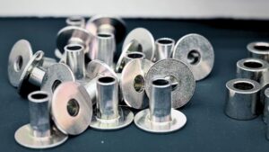 Small, shiny metal pieces with cylindrical bodies and flat bases scattered on a dark surface.