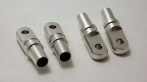 Quatre petites charnières métalliques avec connecteurs cylindriques et trous sur une surface plane.