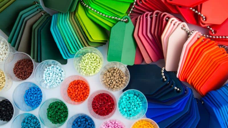 Colorful plastic pellets in clear cups beside assorted color sample keychains.