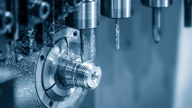 CNC machine drilling into a metal cylinder, metal shavings scattered around the workpiece.