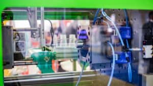 Injection molding machine close-up making a clear plastic part, with visible mechanical parts and control wires.