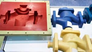 Su un tavolo ci sono stampi per valvole industriali rossi, blu e gialli; quello rosso è aperto per rivelare la cavità interna.