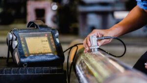 Close-up of a technician using a portable ultrasonic testing device to inspect a metal casting, ensuring quality and defect detection in the die casting process.