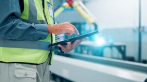 Factory worker using a tablet to monitor manufacturing processes for improved efficiency and quality control.